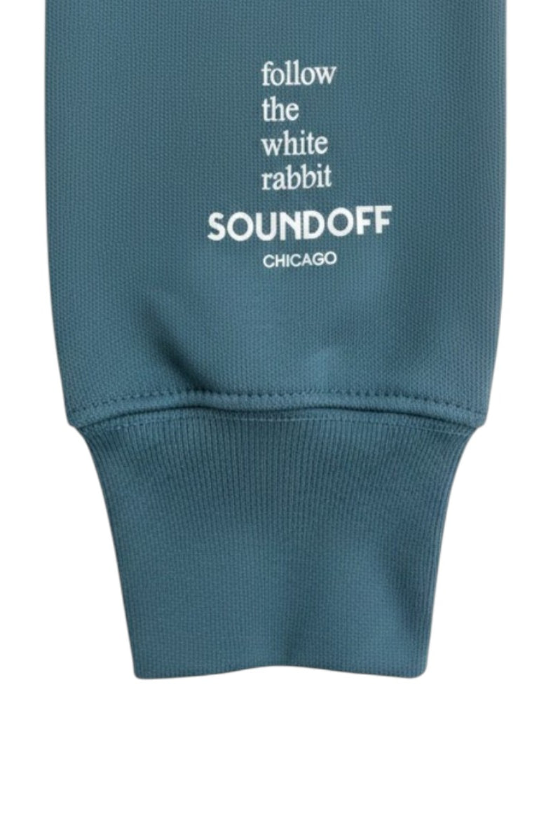 Close-up of the left sleeve on the Heather Teal Bad Bunny Headphones Raglan Sweatshirt, showing the stacked, left-justified "Follow the White Rabbit" text print above the cuff.