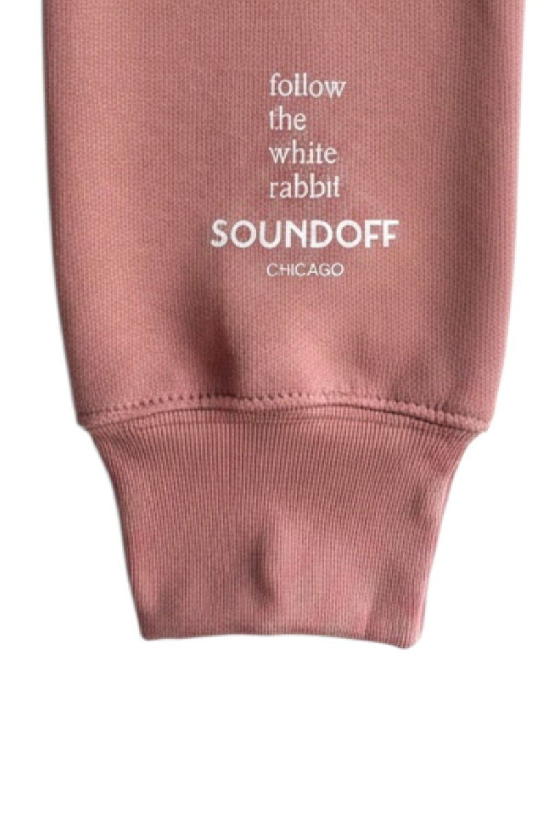 Close-up of the left sleeve on the Mauve Bad Bunny Headphones Raglan Sweatshirt, showing the stacked, left-justified "Follow the White Rabbit" text print above the cuff.