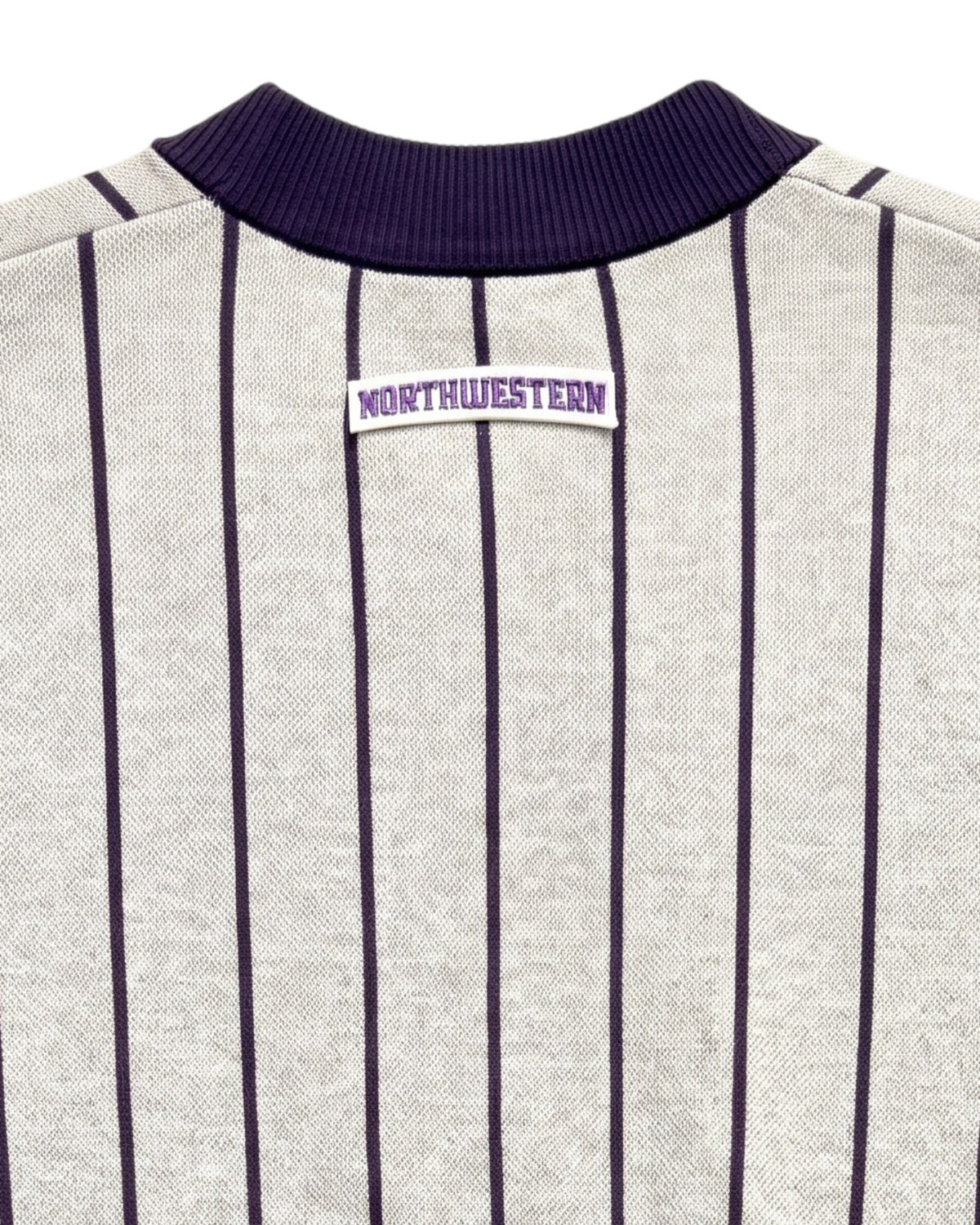 Close up of light grey and purple Northwestern University heritage pinstripe cardigan knit sweater with arched white crest patch with NORTHWESTERN embroidered in purple sewn onto the upper center back below the collar.