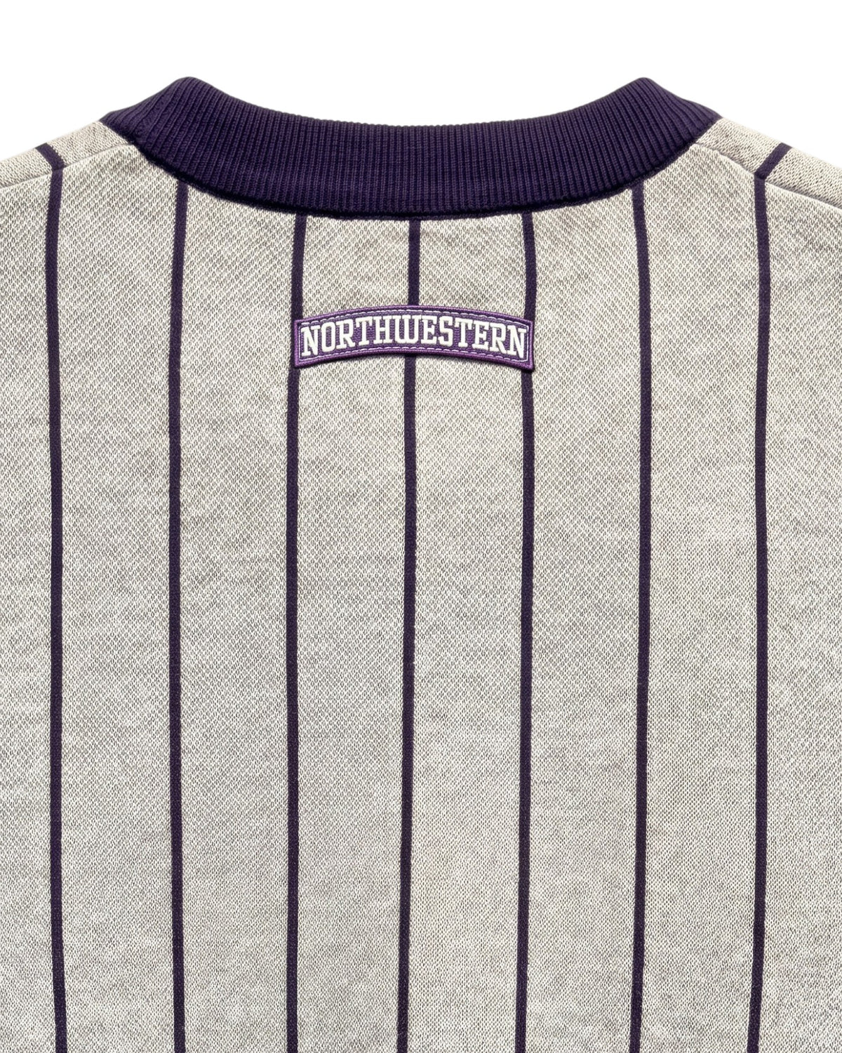 Close up of light grey and purple Northwestern University heritage pinstripe classic crewneck knit sweater with arched purple crest patch with NORTHWESTERN embroidered in white sewn onto the upper center back below the collar.