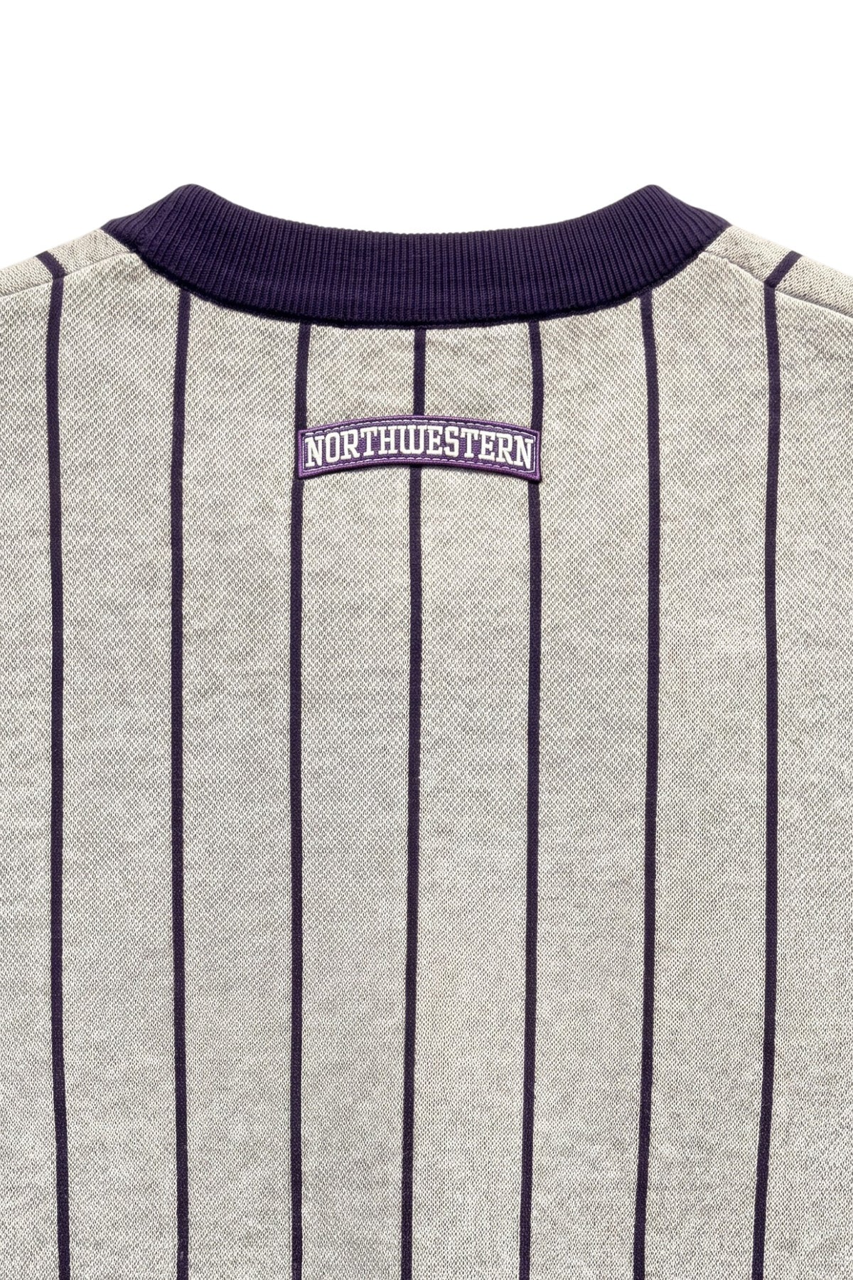 Close up of light grey and purple Northwestern University heritage pinstripe classic crewneck knit sweater with arched purple crest patch with NORTHWESTERN embroidered in white sewn onto the upper center back below the collar.