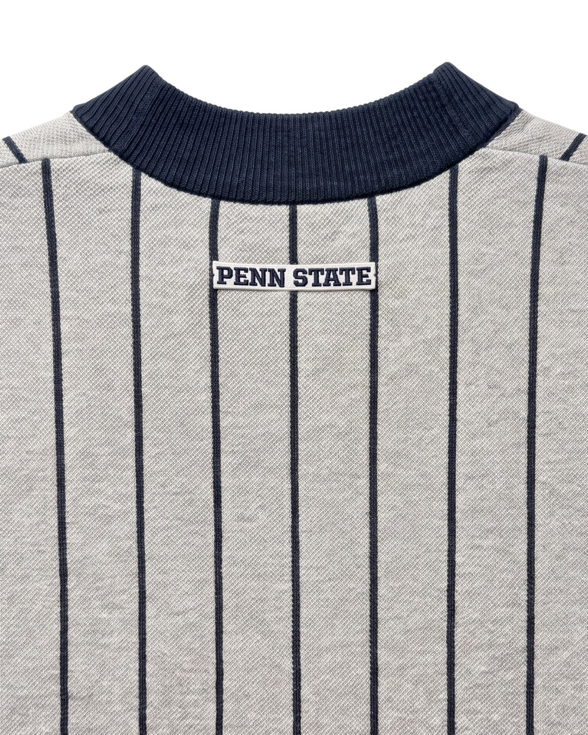 Penn State University block letter embroidered iron-on crest patch in navy and white sewn onto upper back below collar of light grey and navy pinstripe classic crewneck knit sweater