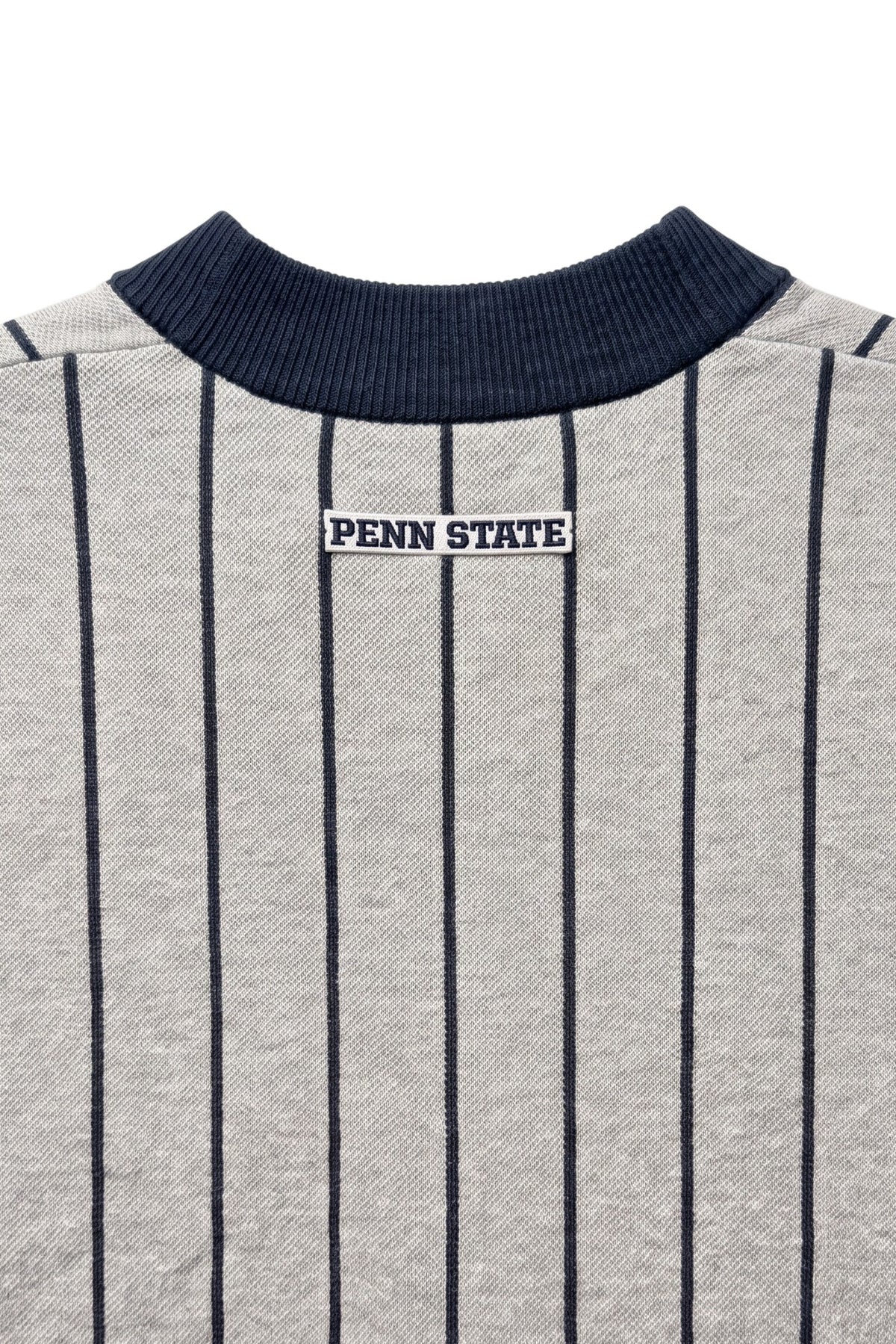 Penn State University block letter embroidered iron-on crest patch in navy and white sewn onto upper back below collar of light grey and navy pinstripe classic crewneck knit sweater