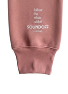 Close-up of the left sleeve on the Mauve Bad Bunny Headphones Raglan Sweatshirt, showing the stacked, left-justified "Follow the White Rabbit" text print above the cuff.
