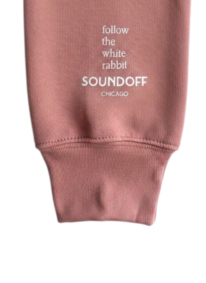 Close-up of the left sleeve on the Mauve Bad Bunny Headphones Raglan Sweatshirt, showing the stacked, left-justified "Follow the White Rabbit" text print above the cuff.