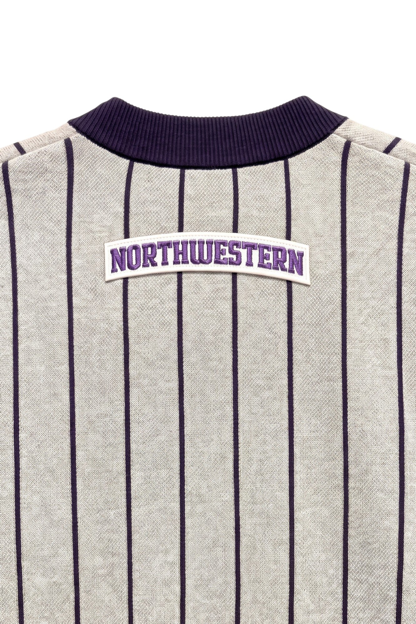 Close up of light grey and purple Northwestern University heritage pinstripe classic crewneck knit sweater with arched white varsity patch with NORTHWESTERN embroidered in purple sewn onto the upper center back below the collar.
