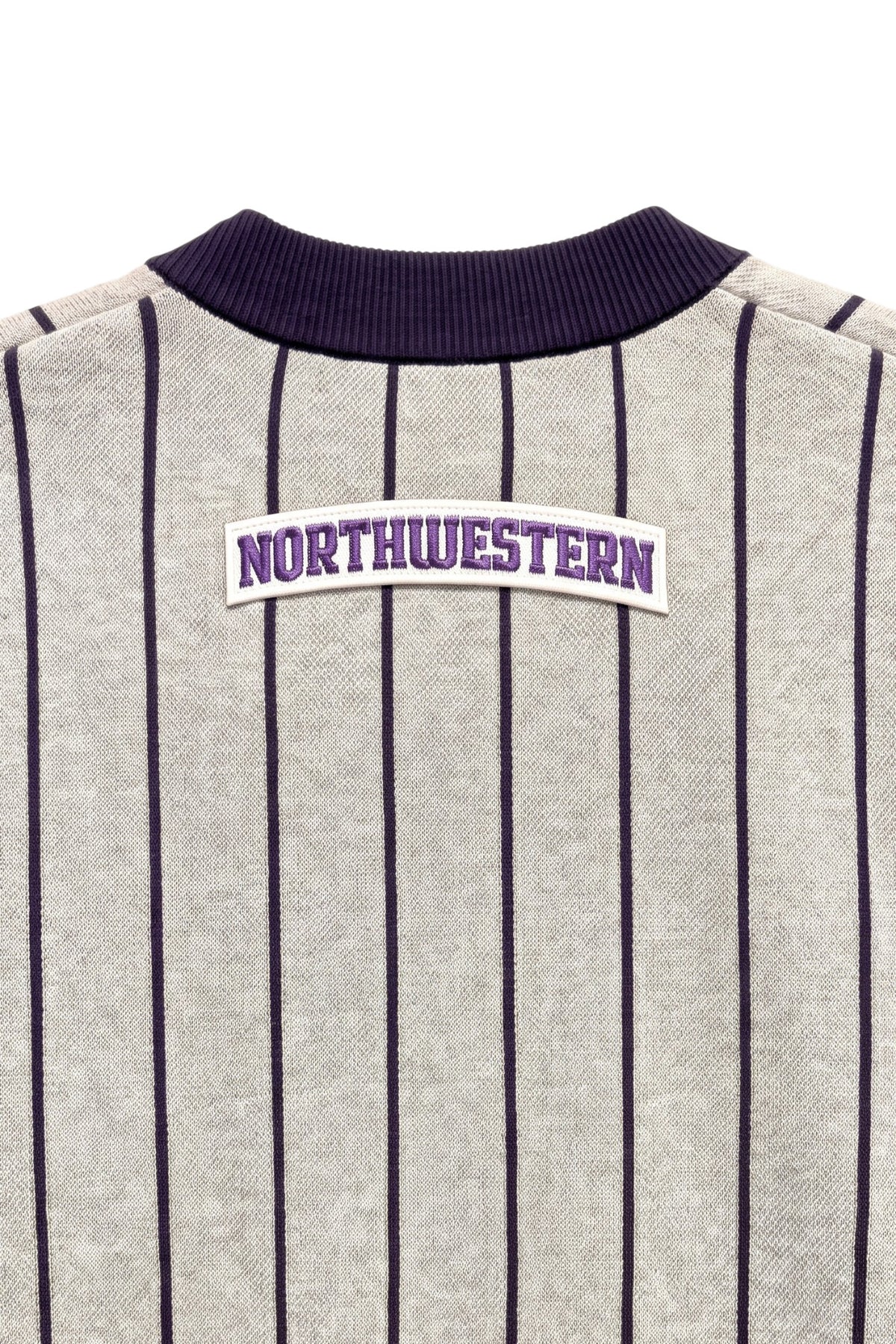 Close up of light grey and purple Northwestern University heritage pinstripe classic crewneck knit sweater with arched white varsity patch with NORTHWESTERN embroidered in purple sewn onto the upper center back below the collar.