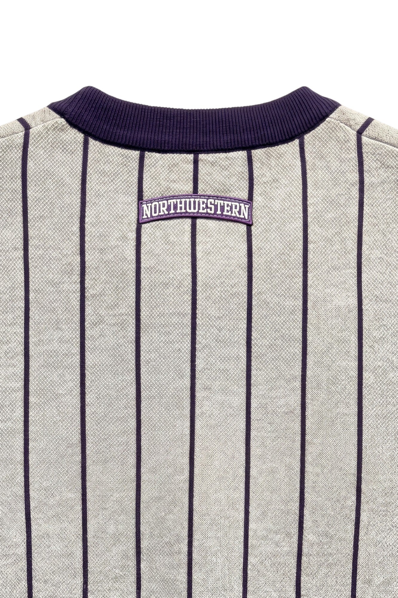 Close up of light grey and purple Northwestern University heritage pinstripe classic crewneck knit sweater with arched purple crest patch with NORTHWESTERN embroidered in white sewn onto the upper center back below the collar.