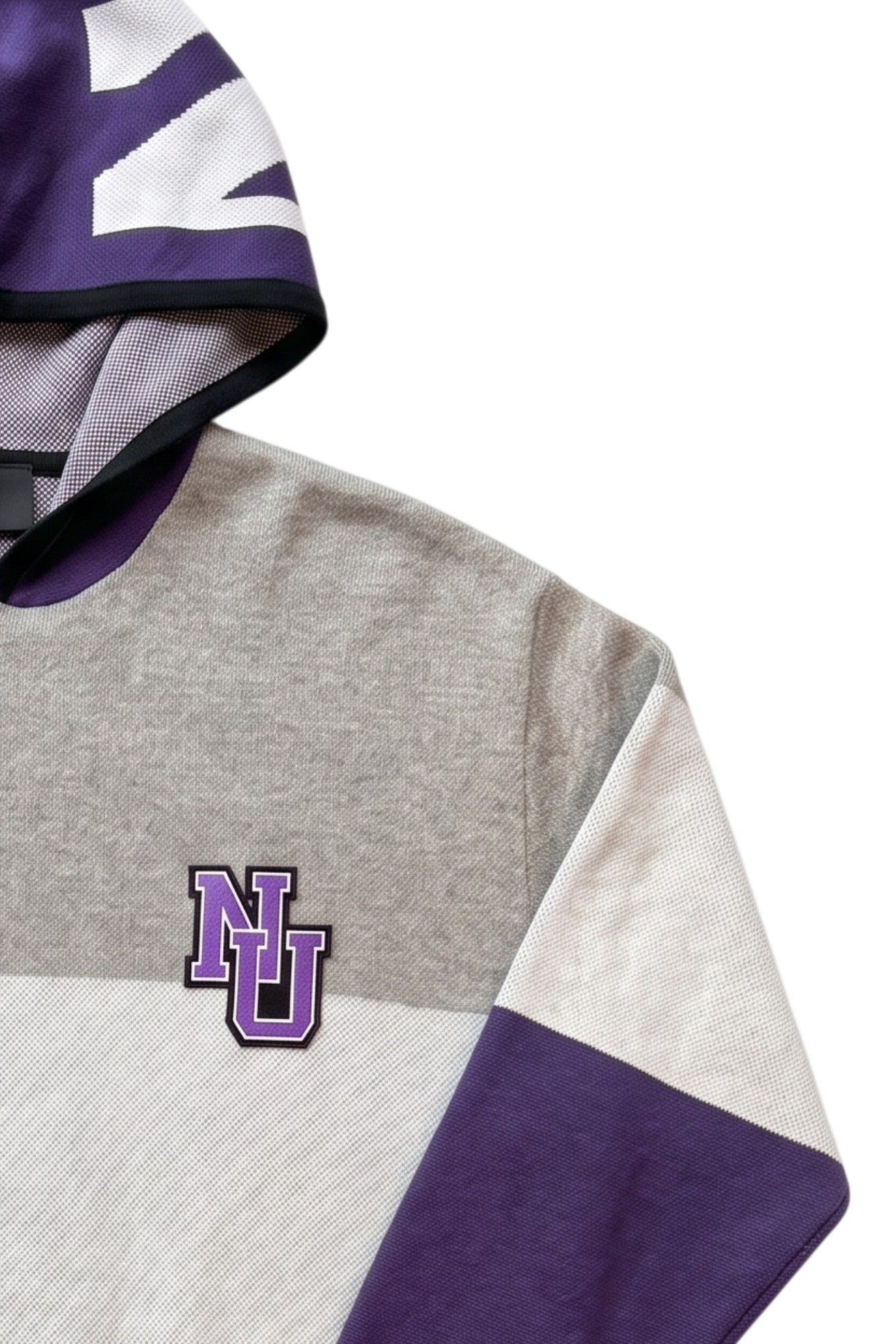 Close up detail of "NU" interlock embroidered crest patch sewn onto Northwestern University purple, white, and light grey striped hooded knit sweater. 