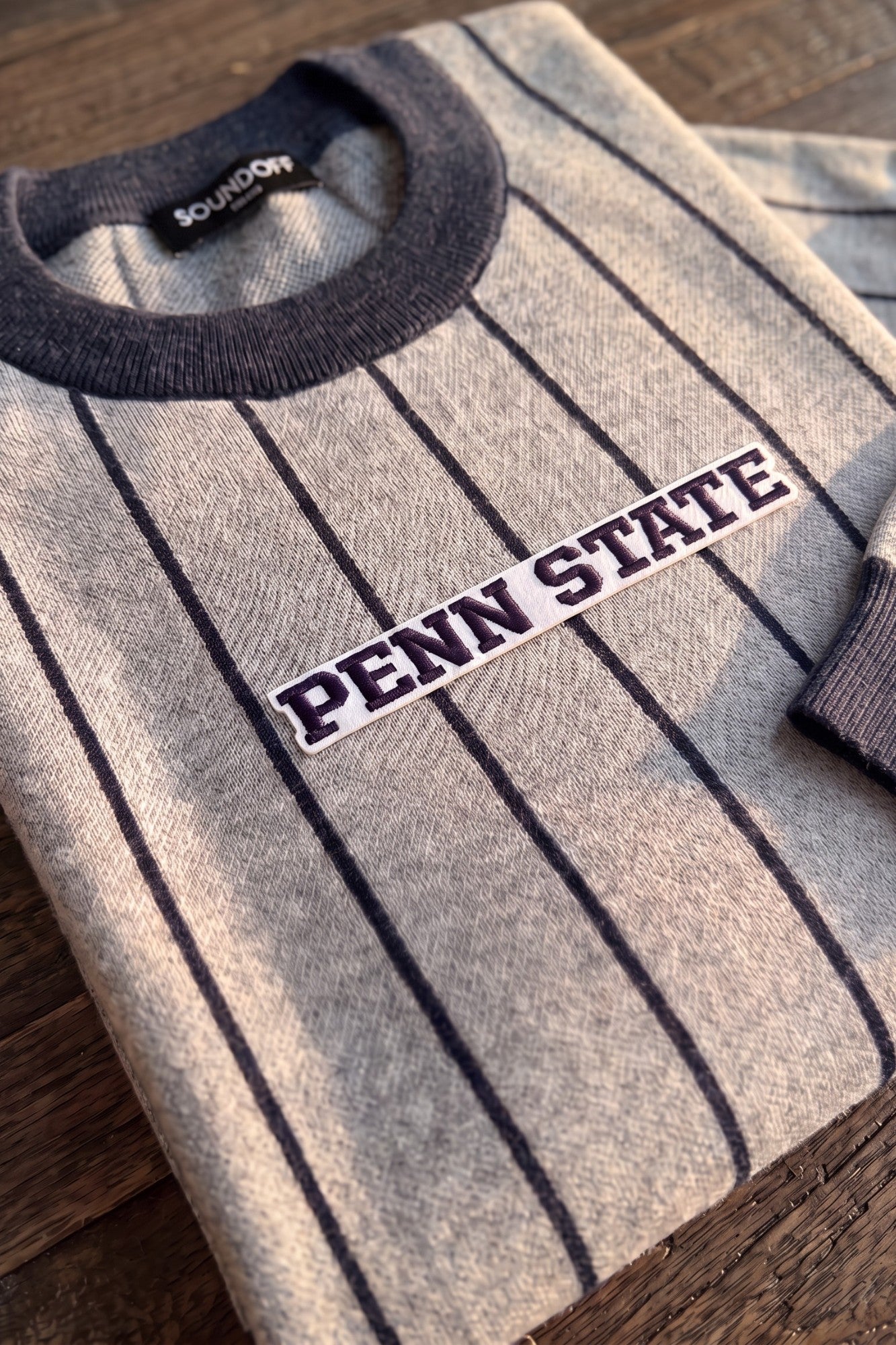 Penn State University block letter embroidered iron-on varsity patch in navy and white sewn onto center front chest of light grey and navy pinstripe classic crewneck knit sweater