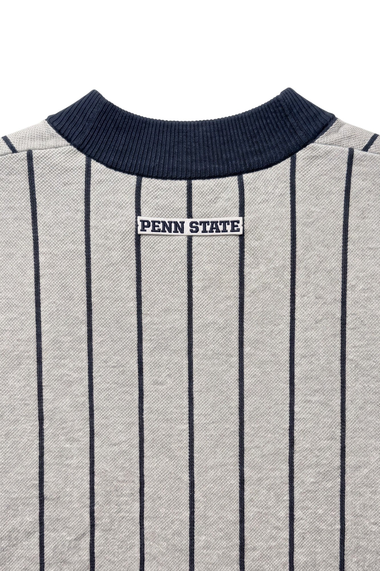 Penn State University block letter embroidered iron-on crest patch in navy and white sewn onto upper back below collar of light grey and navy pinstripe classic crewneck knit sweater