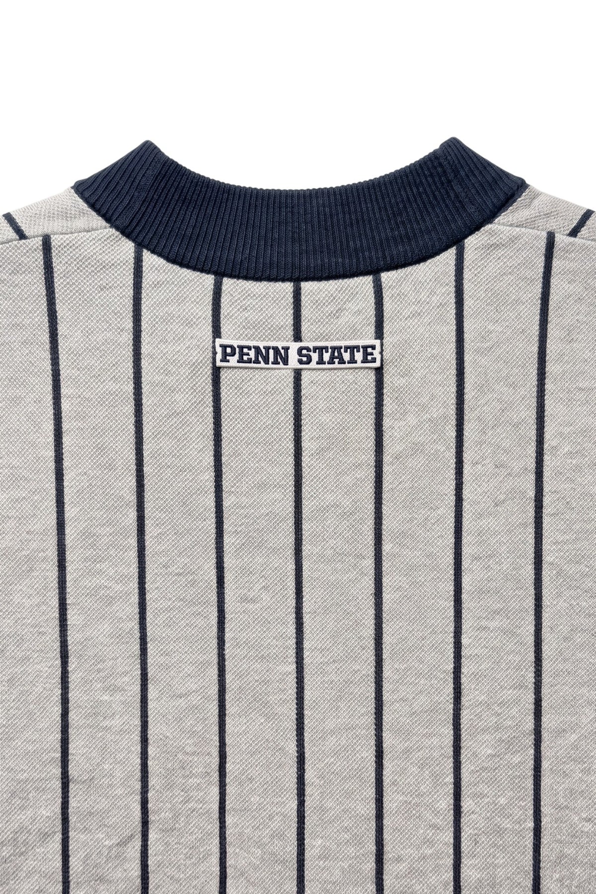 Penn State University block letter embroidered iron-on crest patch in navy and white sewn onto upper back below collar of light grey and navy pinstripe classic crewneck knit sweater