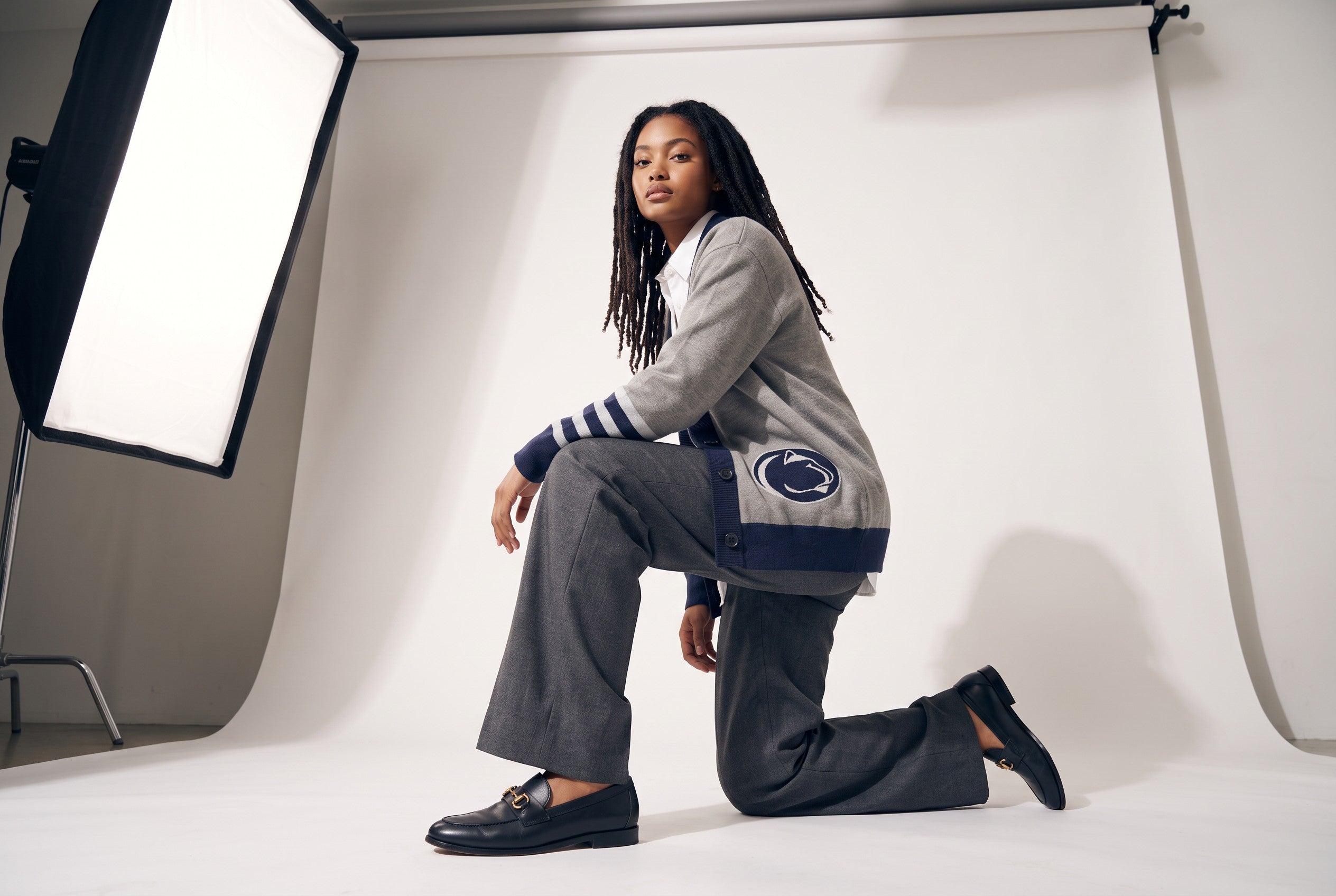 Female model wearing Penn State University letterman band cardigan with Nittany Lion embroidered applique varsity patch sewn onto lower front side.