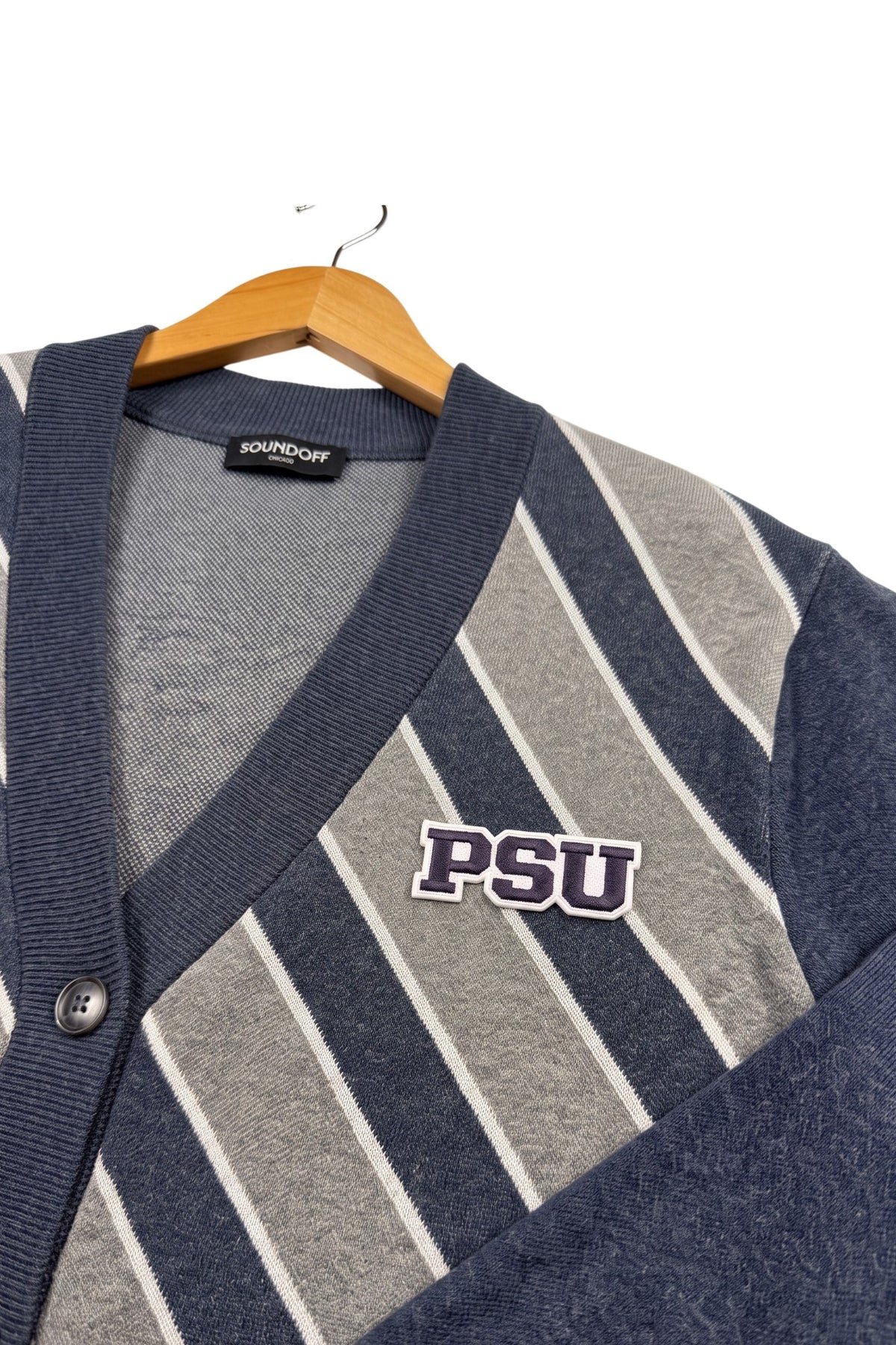 Penn State PSU crest embroidered patch in navy and white sewn onto left chest of navy cardigan knit sweater with white and light grey repp stripes.