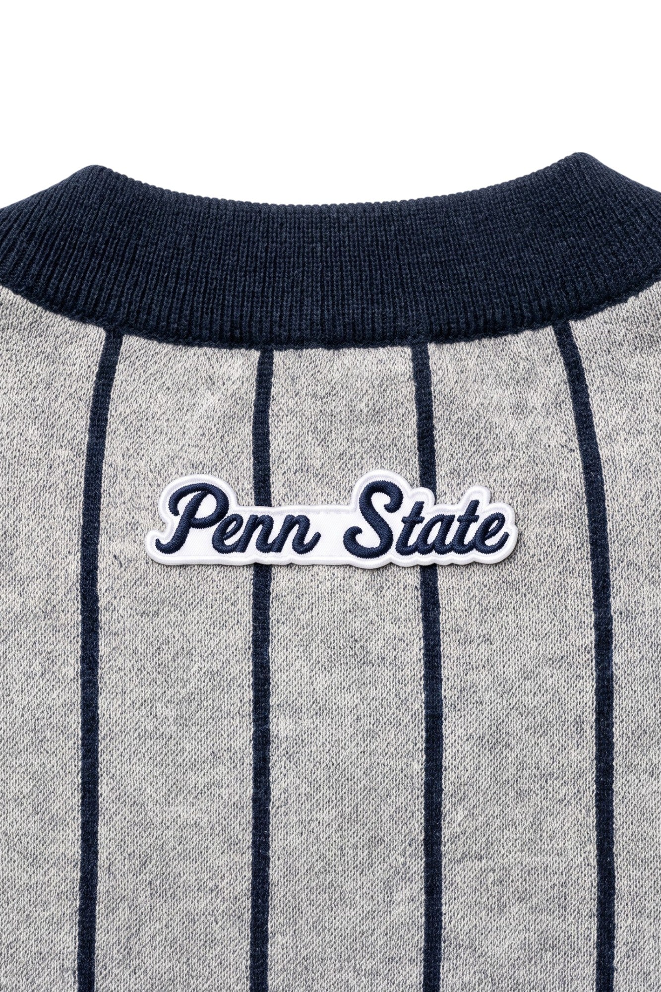 Penn State University script letter crest patch sewn onto upper back below collar of light grey cardigan knit sweater with navy pinstripes and trim.