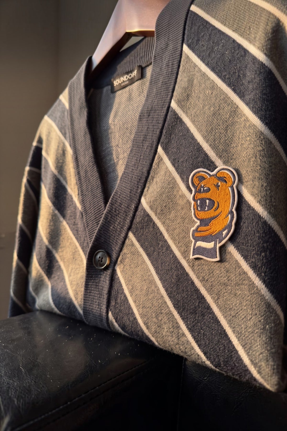 Penn State Nittany Lion head embroidered crest patch with scarf in brown, navy and white sewn onto left chest of navy knit cardigan sweater with light grey and white repp stripes.