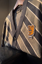 Penn State Nittany Lion head embroidered crest patch with scarf in brown, navy and white sewn onto left chest of navy knit cardigan sweater with light grey and white repp stripes.